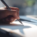 A hand holds a pen over a sheet of paper, ready to write a letter.